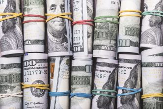American one hundred dollar bill rolls, with colourful rubber bands, lined up in two rows.