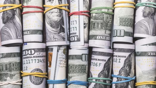 American one hundred dollar bill rolls, with colourful rubber bands, lined up in two rows.