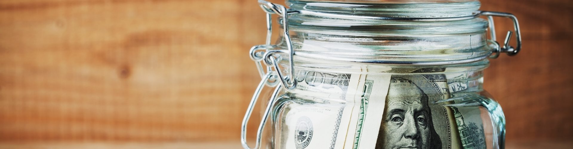 Dollar bills in glass jar on rustic table. Saving money concept.