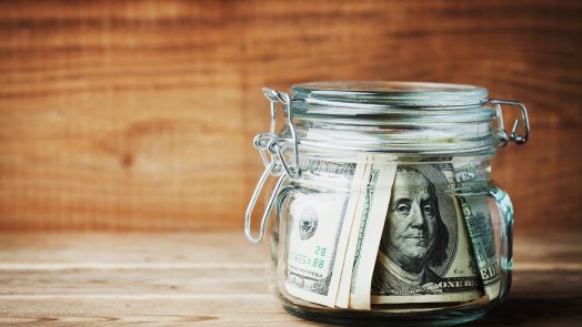 Dollar bills in glass jar on rustic table. Saving money concept.
