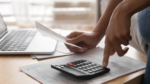 African woman holding paper bills using calculator, close up view