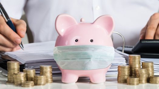 Businessman Calculating Invoice With Piggybank And Coins At Desk