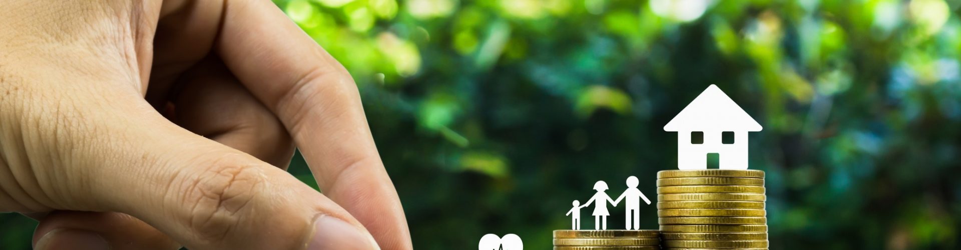 Saving or making money for family life in future concept. A man hand putting coin into rising stack of coins with heart, family and small house model on wood table. Depicts sustainable financial goal.
